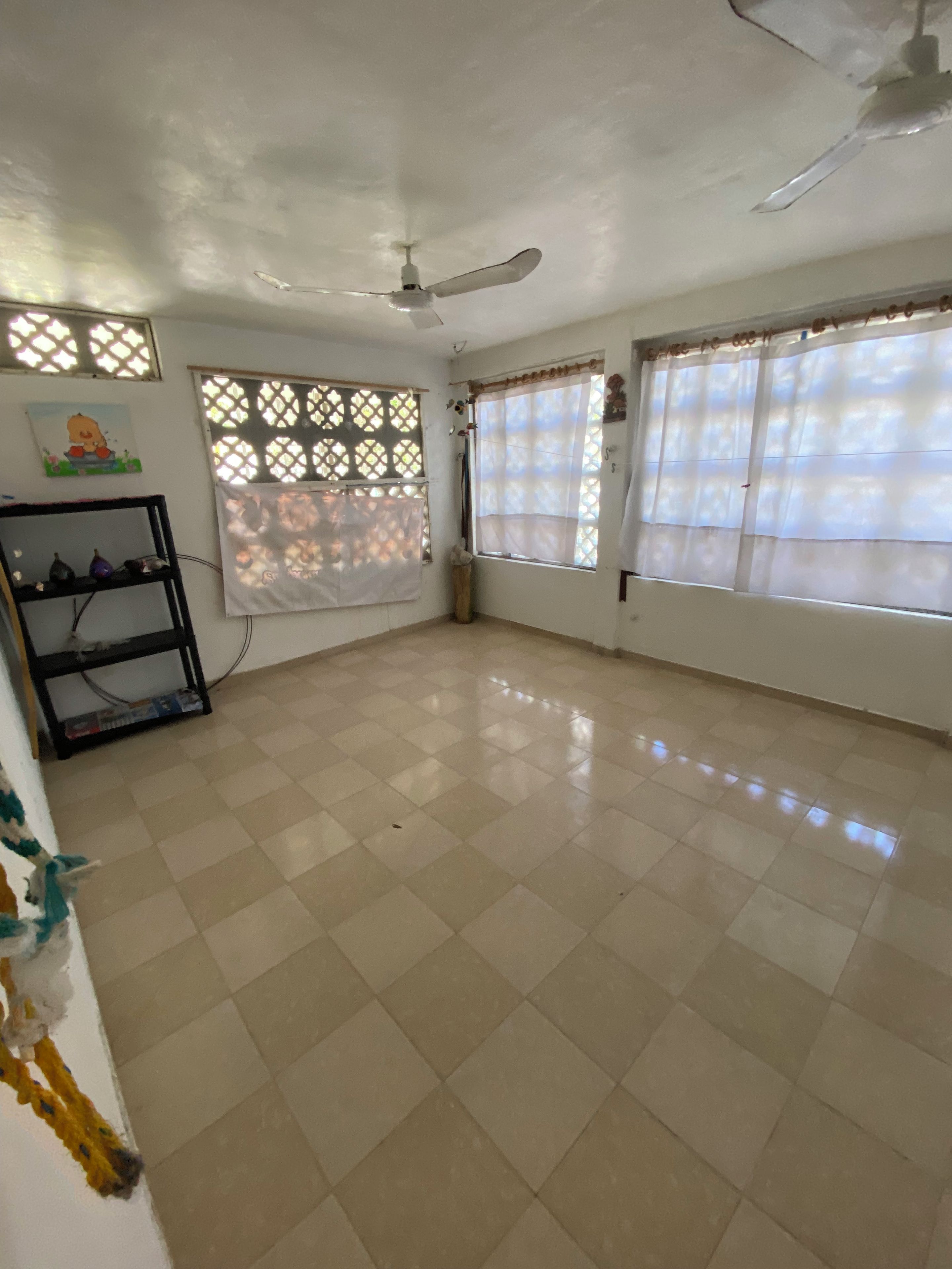 A room with a tiled floor, a ceiling fan, and windows with curtains.