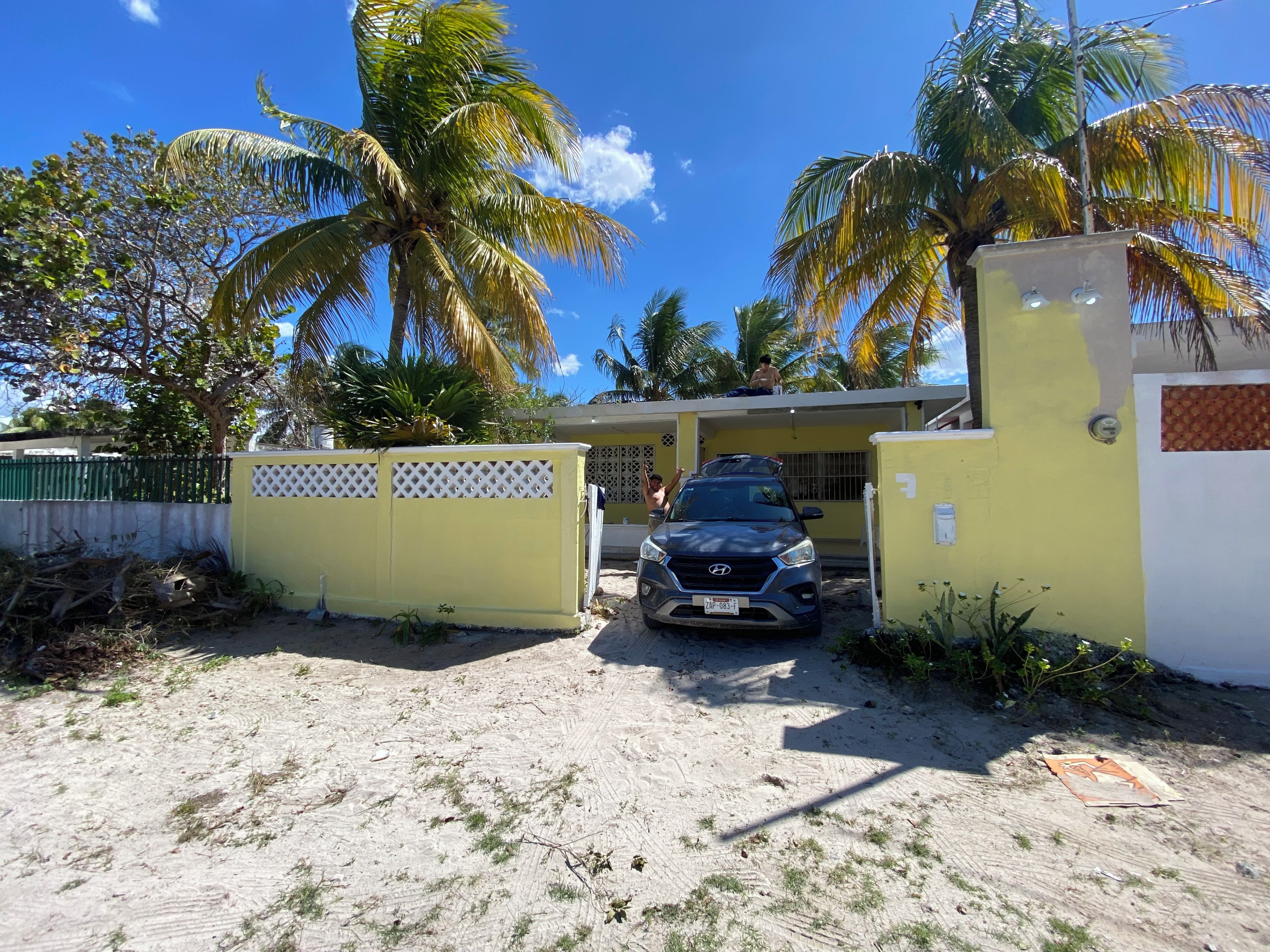 A gated property with a parked vehicle, palm trees, and a clear sky.