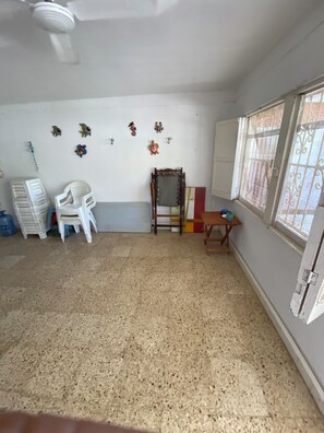 A room with a tiled floor, a chair, a small table, a window with bars, and wall decorations.