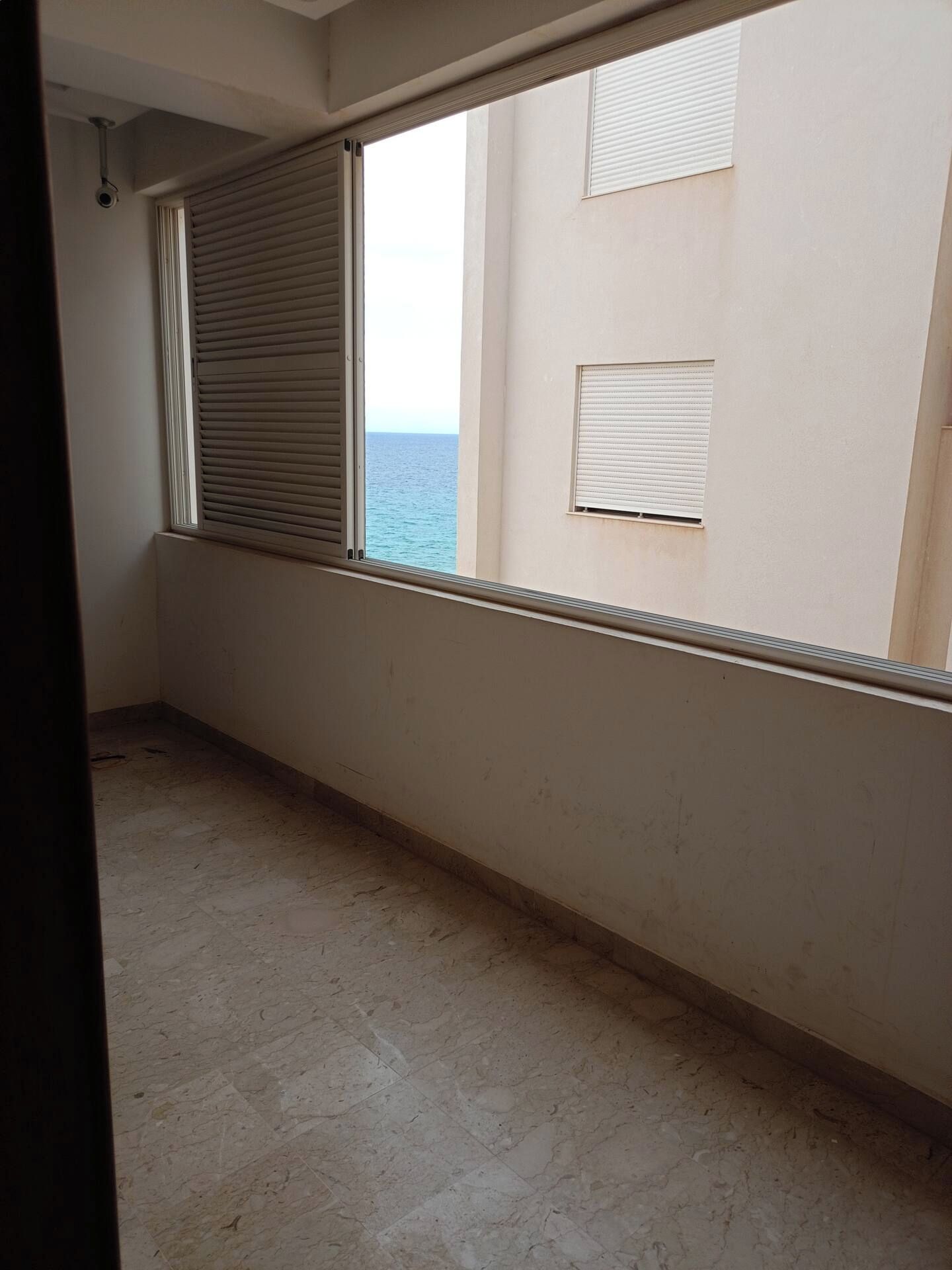 Quarto com uma janela grande, um radiador e vista para o mar.