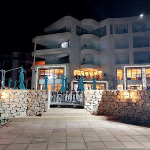 A multi-story hotel with a stone facade, outdoor seating area, and illuminated windows.