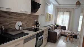 A modern kitchen with a built-in oven, a coffee maker, and a dining area with a sofa and a small round table.