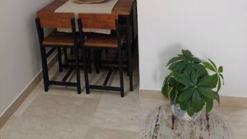 Un coin repas avec une table et des chaises en bois, une étagère murale agrémentée d’objets décoratifs et un tableau abstrait aux couleurs vives.