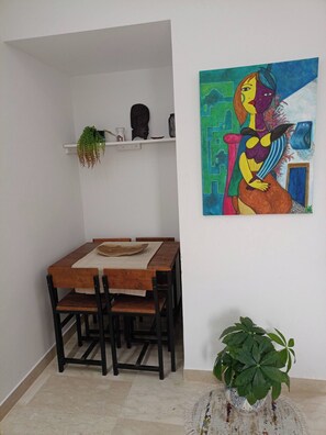 A dining area with a wooden table and chairs, a wall-mounted shelf with decorative items, and a colorful abstract painting.
