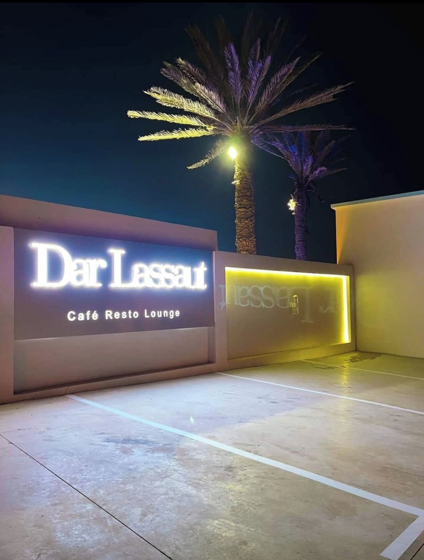 A nighttime entrance to Dar Lassaut Café Resto Lounge with illuminated signage and palm trees.