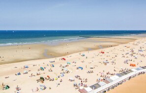Uma praia com vários espreguiçadeiras e guarda-sóis, céu claro e o oceano ao fundo.