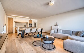 A modern living room with a sofa, two coffee tables, and a dining area with chairs and a kitchen in the background. - 3 bedroom luxurious apartment in Oostende (Oostende)