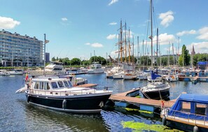 En småbåtshamn med olika typer av båtar förtöjda, en modern byggnad i bakgrunden och en klar himmel.