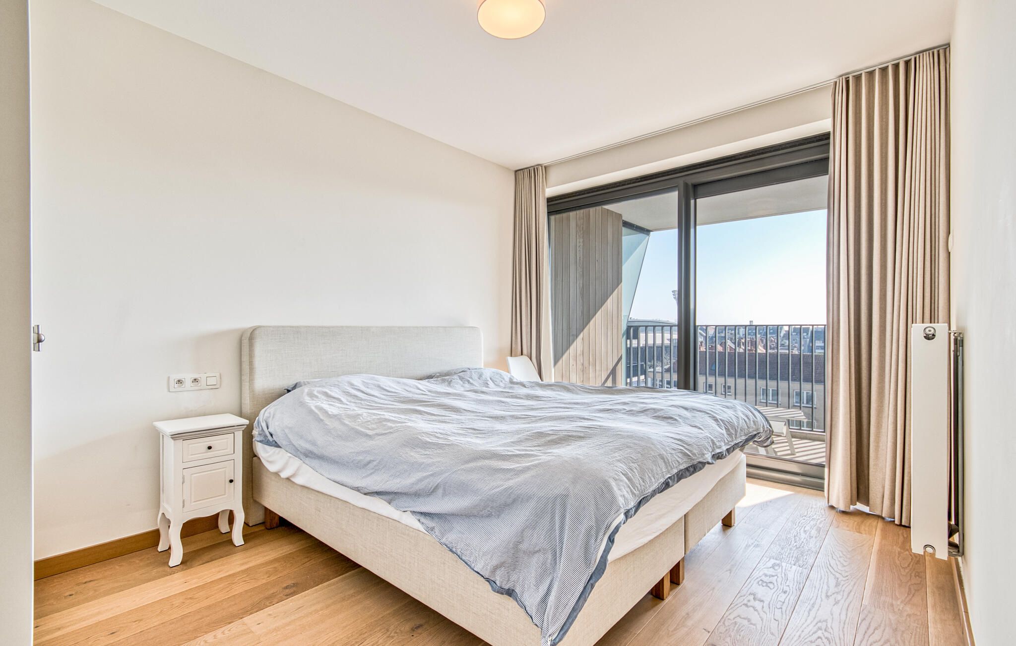 A bedroom with a bed, bedside table, and a view of the outside.
