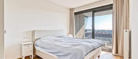 Ein Schlafzimmer mit Bett, Nachttisch und Blick ins Freie.