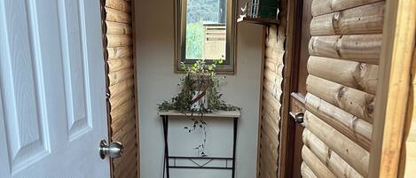 A hallway with a wooden door labeled 'OUR HOME,' a small table with a plant, and a window with a view.