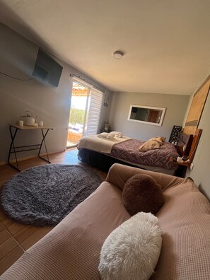 A bedroom with a bed, a sofa, a small table, and a window.