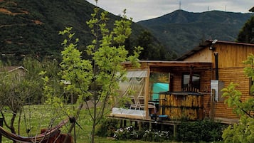A wooden cabin with a deck, surrounded by a grassy area and trees.