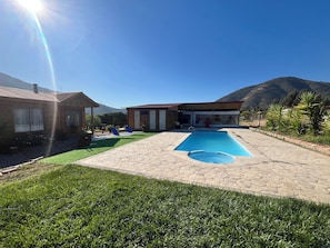 Imóvel residencial com piscina, varanda coberta e montanhas ao fundo.
