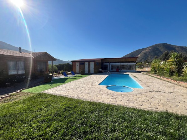 A residential property with a swimming pool, a covered patio, and a mountain backdrop.