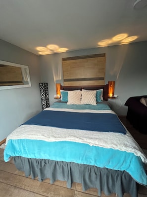 Quarto com cama, duas luminárias de cabeceira, painel de cabeceira em madeira e uma obra de arte na parede.
