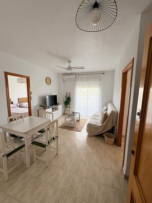 A modern living room with a dining area, a ceiling fan, a TV, and a large window with curtains. - Sun & Beach in the Heart of Torrevieja (Torrevieja)