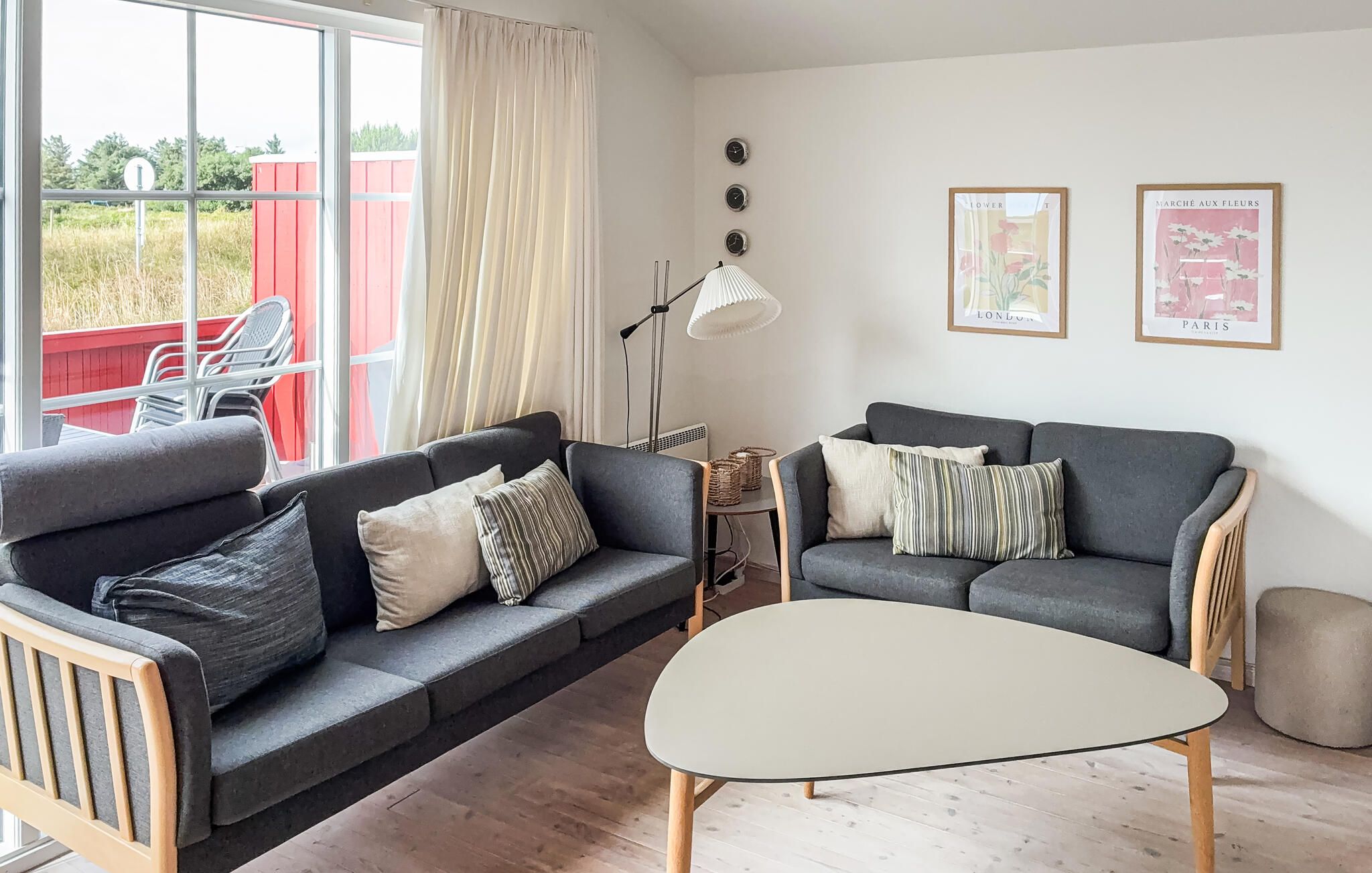 A living room with a grey sofa, a round coffee table, and a red outdoor area visible through the window.