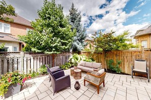 Un'area patio con mobili da esterno, una recinzione in legno e diverse piante.