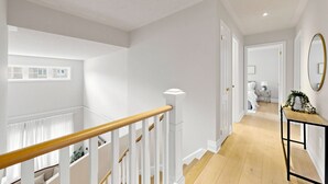 Ein modernes Interieur mit einer Treppe, einem Flur, der zu einem Schlafzimmer führt, und einem Essbereich mit Tisch und Stühlen.