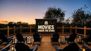 Un espace extérieur aménagé pour les projections de films, avec une terrasse en bois, des sièges et un grand écran diffusant des films dans le cadre de l'événement « CINÉMA À LA BELLE ÉTOILE ».