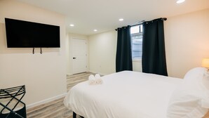 Une chambre d’hôtel avec un lit, un téléviseur fixé au mur, un bureau et une fenêtre avec des rideaux.