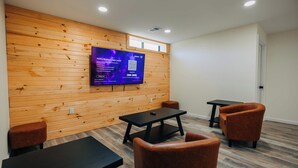 Une pièce avec un mur en bois, un téléviseur à écran plat fixé au mur, une table noire, deux chaises marron et une petite table noire.