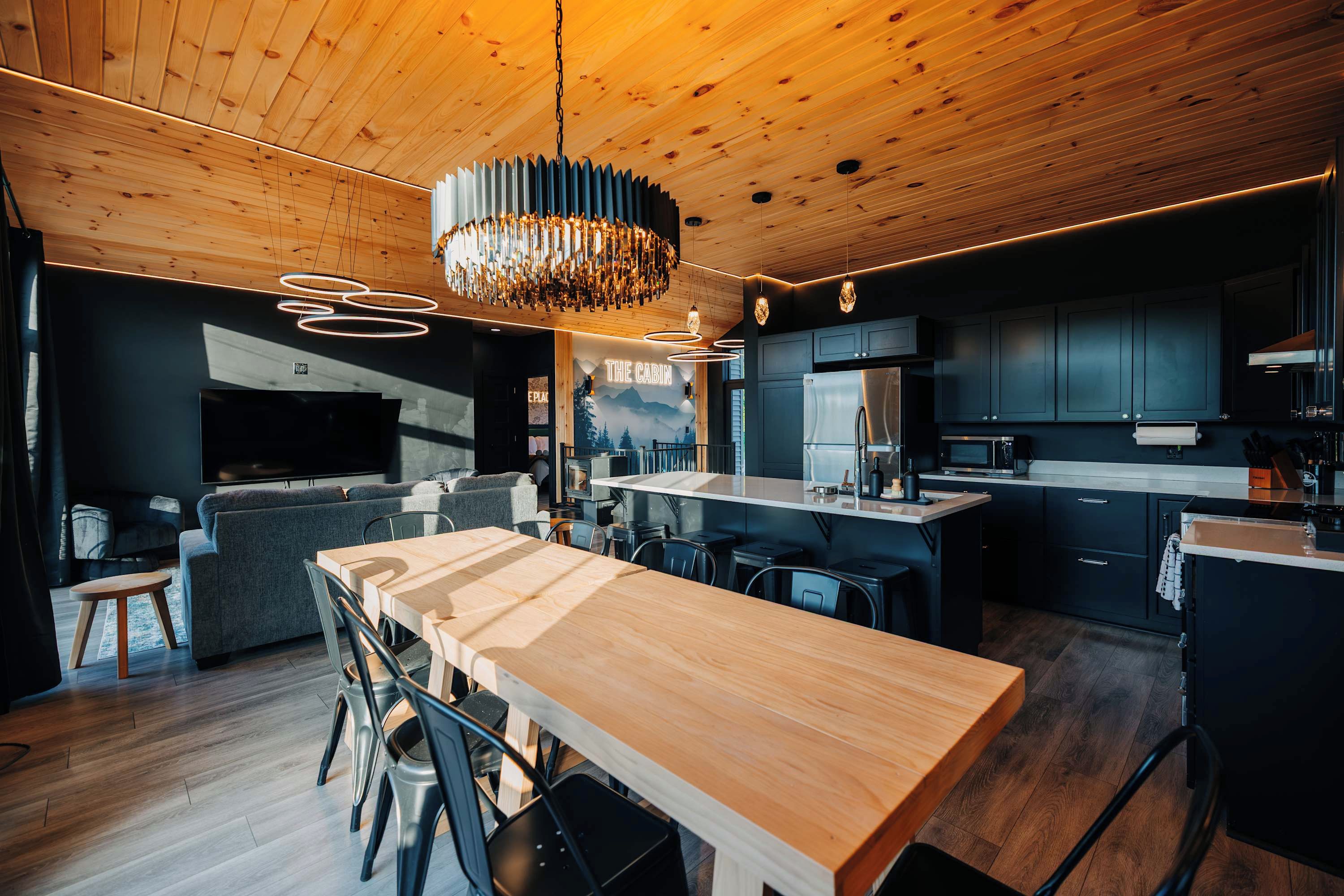 Une cuisine moderne avec des meubles de couleur sombre, une table à manger en bois et un lustre.