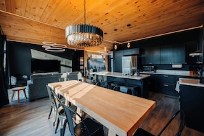 A modern kitchen with dark cabinetry, a wooden dining table, and a chandelier.