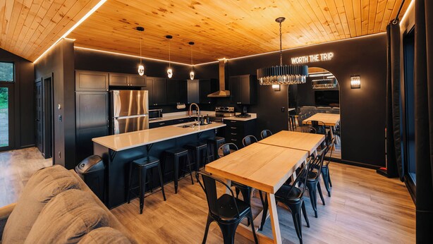 Une cuisine moderne dotée d’un îlot central, de tabourets de bar et d’un coin repas avec une longue table.