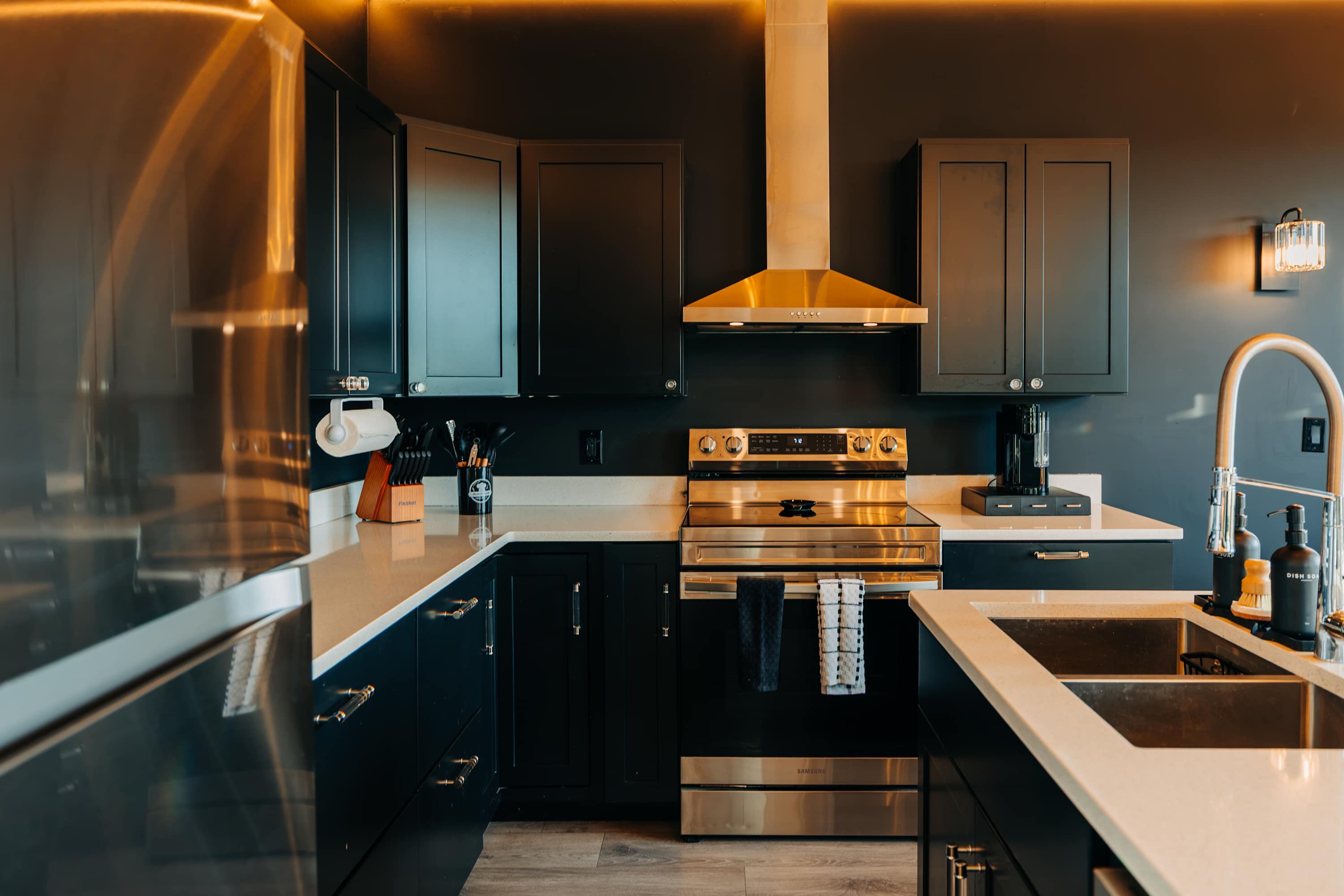 Une cuisine moderne dotée d’appareils électroménagers en acier inoxydable, de meubles de rangement noirs et d’un plan de travail blanc.