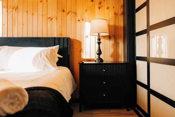 A bedroom with a bed, a nightstand with a lamp, and wooden paneling on the walls.