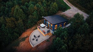 Una casa moderna con terraza, jacuzzi y zona de estar exterior rodeada de un bosque denso.