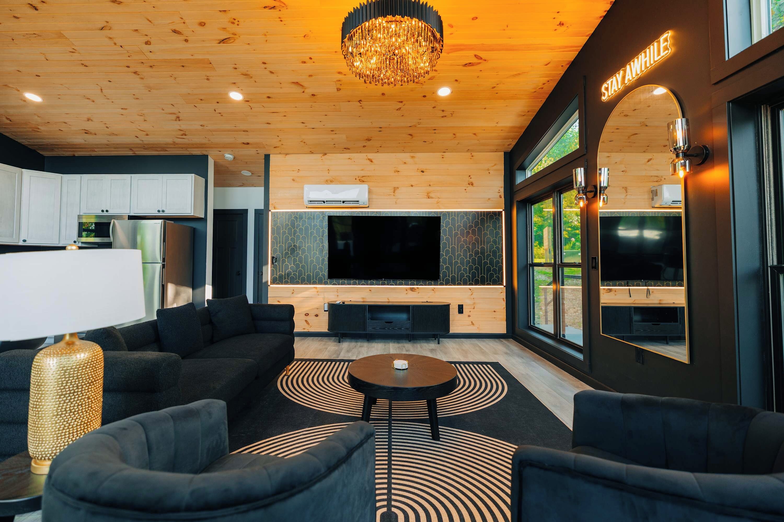 Een moderne woonkamer met een grote televisie, comfortabele zitplaatsen en een kroonluchter.