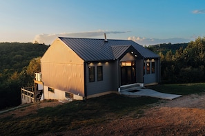 Une petite cabane à un seul étage, avec un toit en métal, un porche à l’avant et une enseigne sur laquelle on peut lire « The Cabin ».