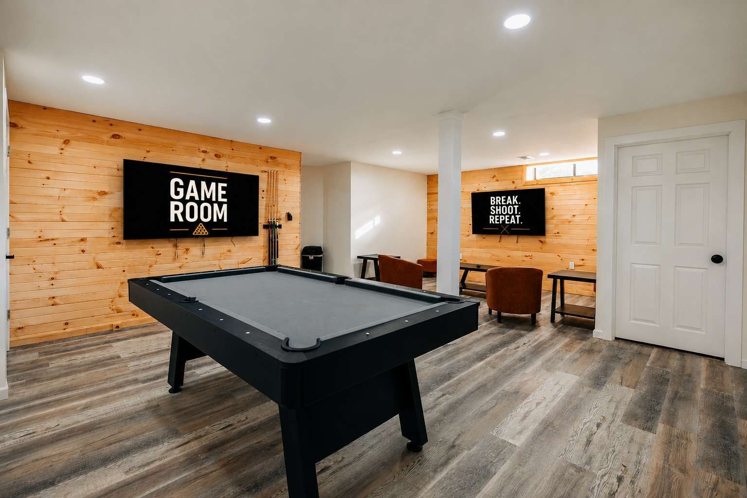 A game room with a pool table, wooden walls, and two motivational screens.