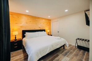 Une chambre avec un mur en bois, un lit avec une literie blanche, une table de chevet avec une lampe et un téléviseur fixé au mur.