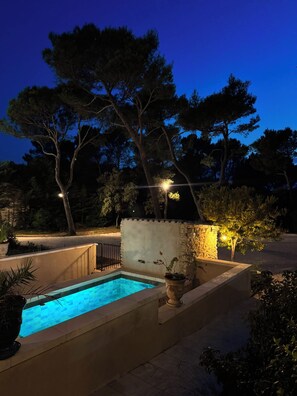A swimming pool with a stone wall and potted plants, surrounded by trees and outdoor lighting. - 🌿 La Bastide de la Colline, an authentic Provençal house with a private pool. (Cavaillon)