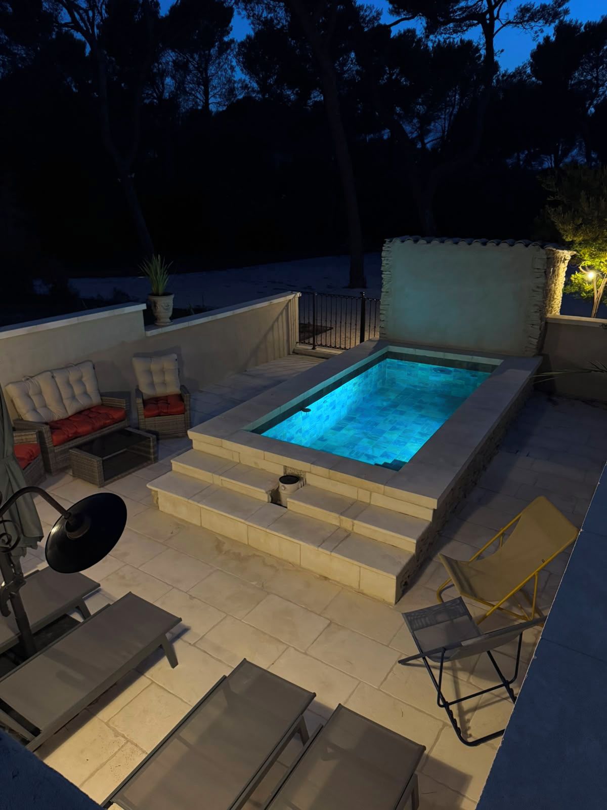 A swimming pool with steps leading into it, surrounded by outdoor furniture and a potted plant.