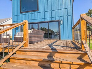 Eine Holzterrasse führt zu einem blauen Gebäude mit einem großen Fenster und einer Tür.