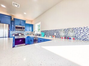 A modern kitchen with blue cabinets, a stainless steel refrigerator, a microwave, and a purple oven. - NEW Longtown Lakefront Retreat | Boat Slip | Game Room | Sleeps 10 (Eufaula)