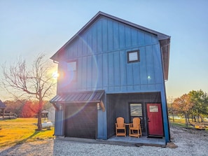 Ein zweistöckiges Gebäude mit Garage, zwei Holzstühlen draußen und einer roter Tür.