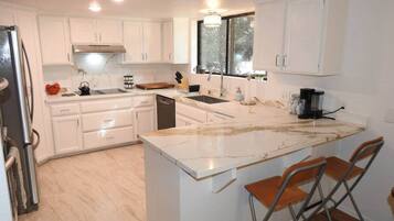 A modern kitchen with white cabinetry, a marble countertop, and a built-in island with bar stools.