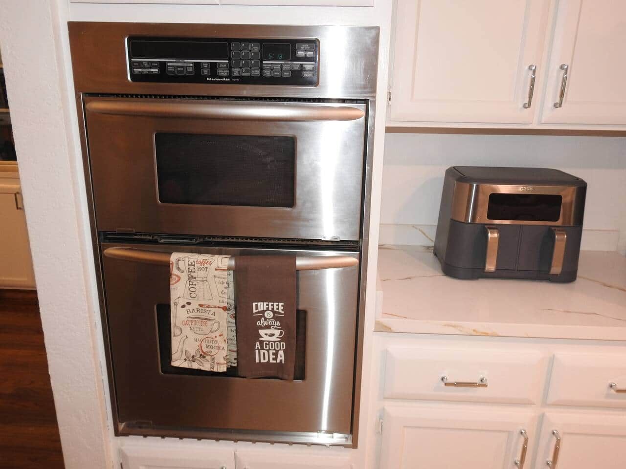 Horno de acero inoxidable con panel de control digital y una toalla con motivos de café colgada.