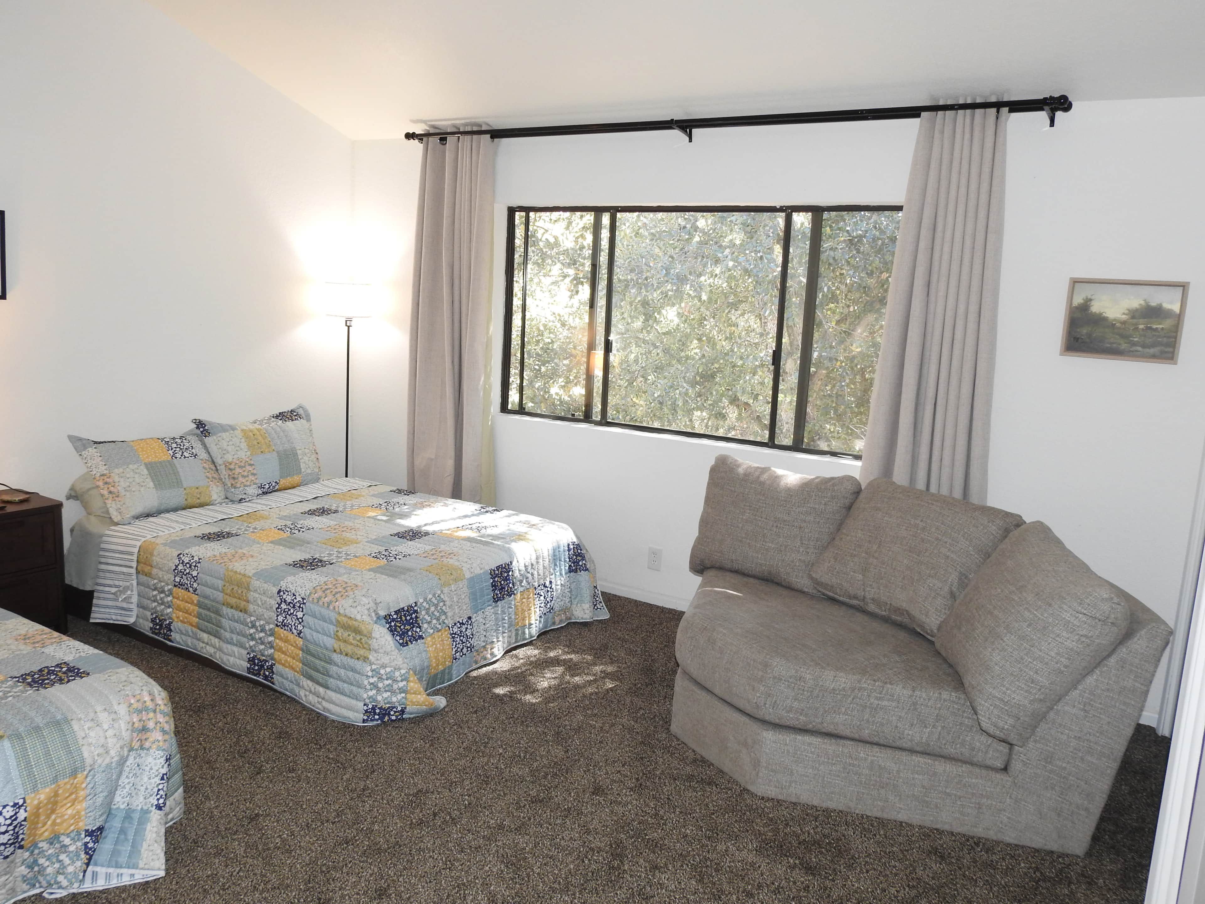 A bedroom with a bed, a sofa, a window, and a lamp.