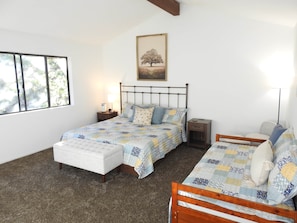 Een slaapkamer met een bed, nachtkastjes, een lamp, een raam en een schilderij aan de muur.