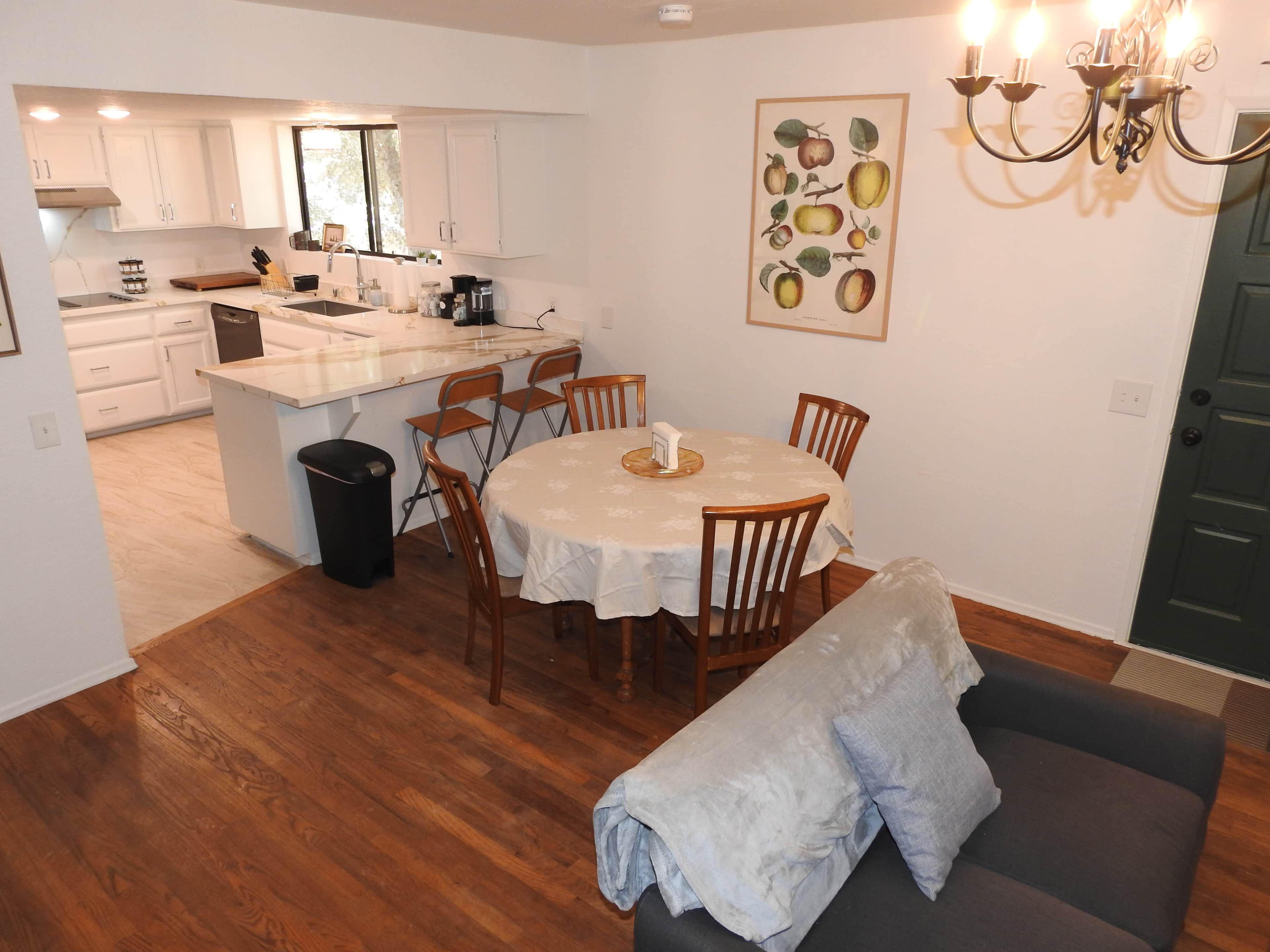 A modern kitchen with white cabinets, a dining area with a round table and chairs, and a living room with a sofa.