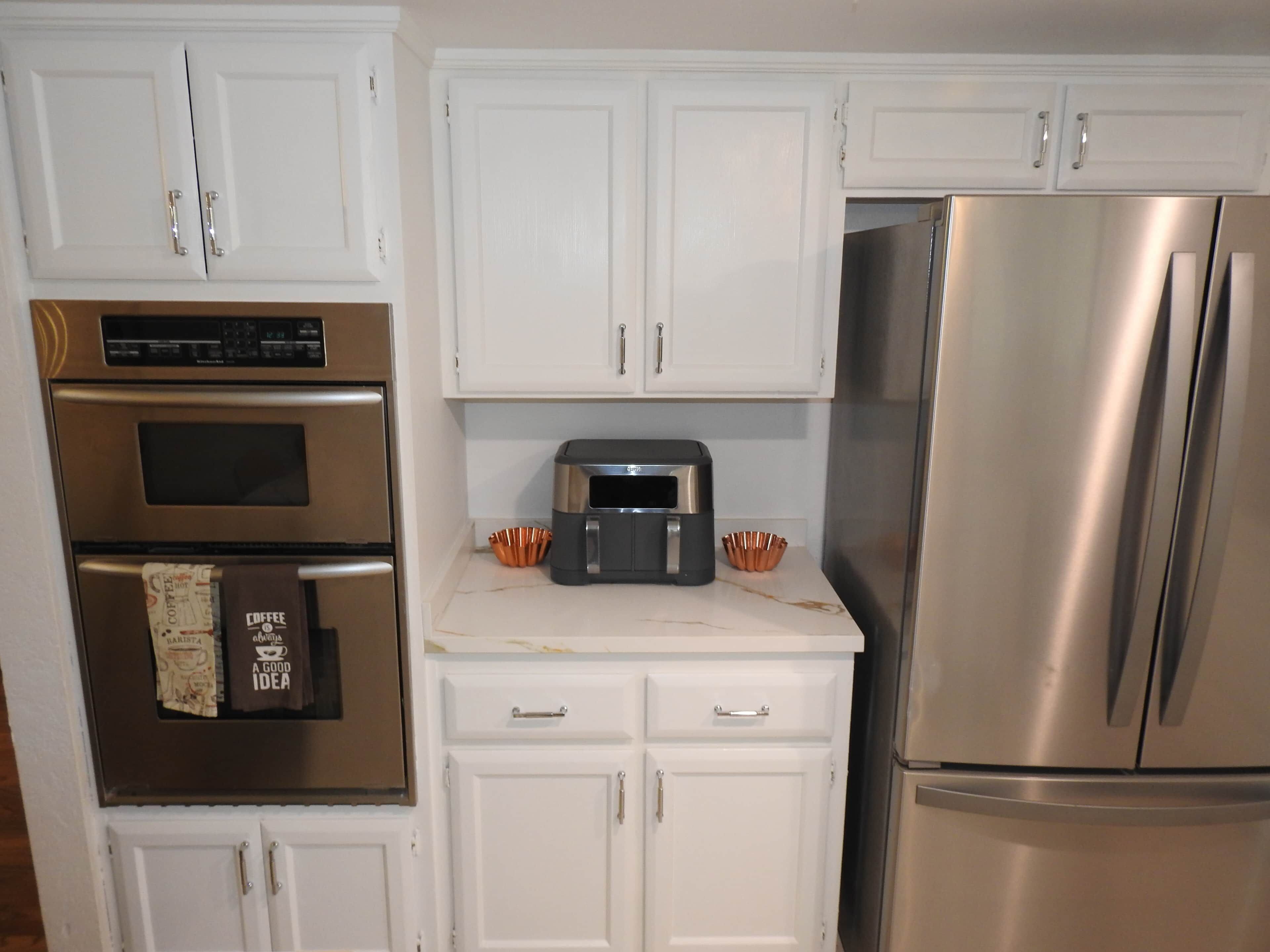 A kitchen with white cabinets, a stainless steel oven, a coffee maker, and a refrigerator.