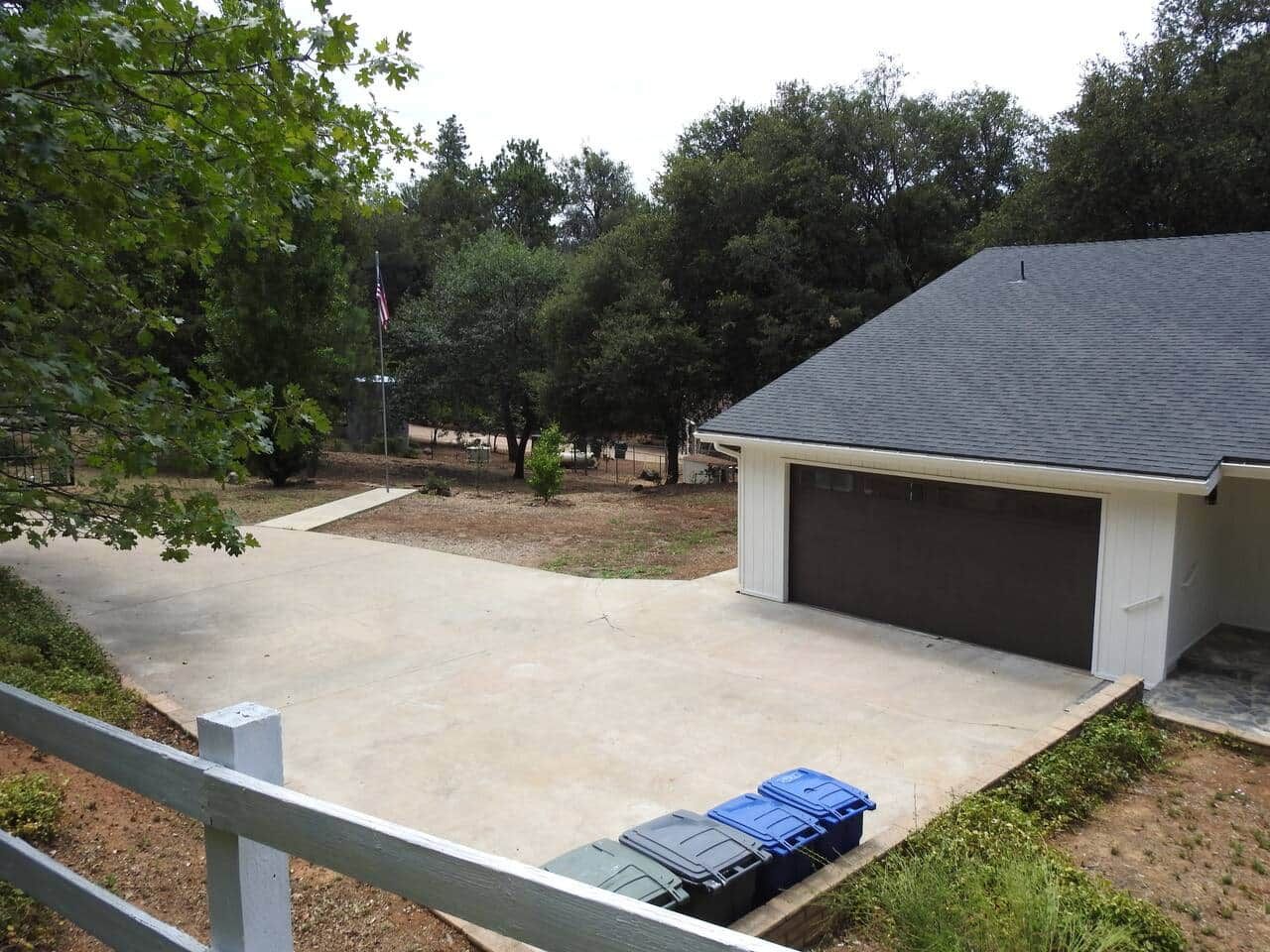 A residential garage with a concrete driveway, a small shed, and a flagpole with an American flag.