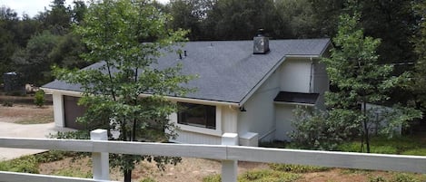 A single-story house with a dark roof, surrounded by a white fence, and trees in the background.